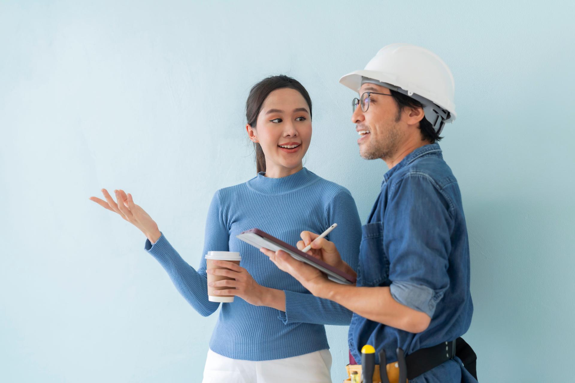 Asian young female architect discussing with japanese male building manager contractor for quality control site inspection and at house construction site in room under renovation project.